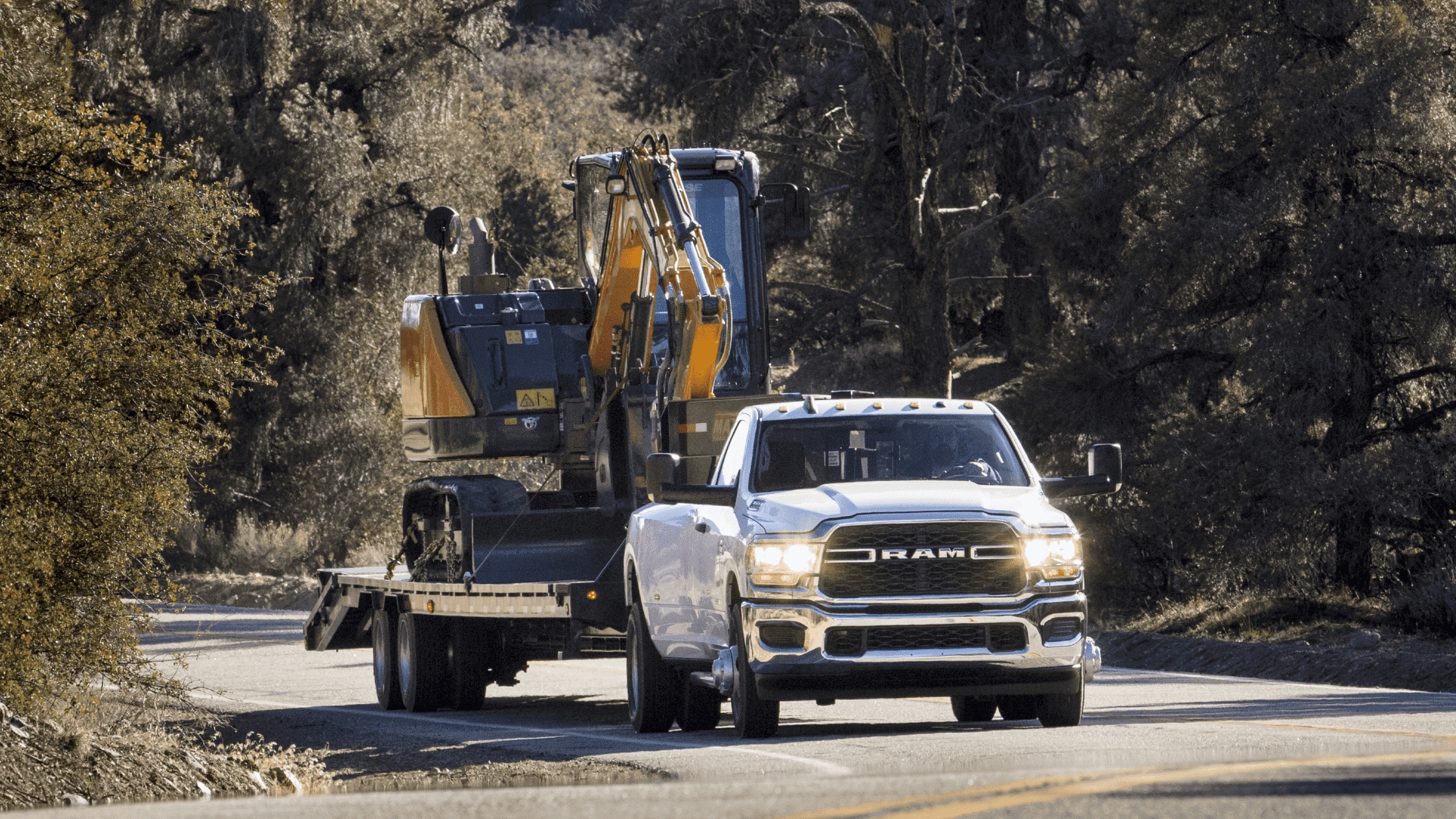 2024 Ram 3500 towing heavy equipment on a rugged road, highlighting its powerful towing capacity, perfect for Naples, FL boaters and RV owners.