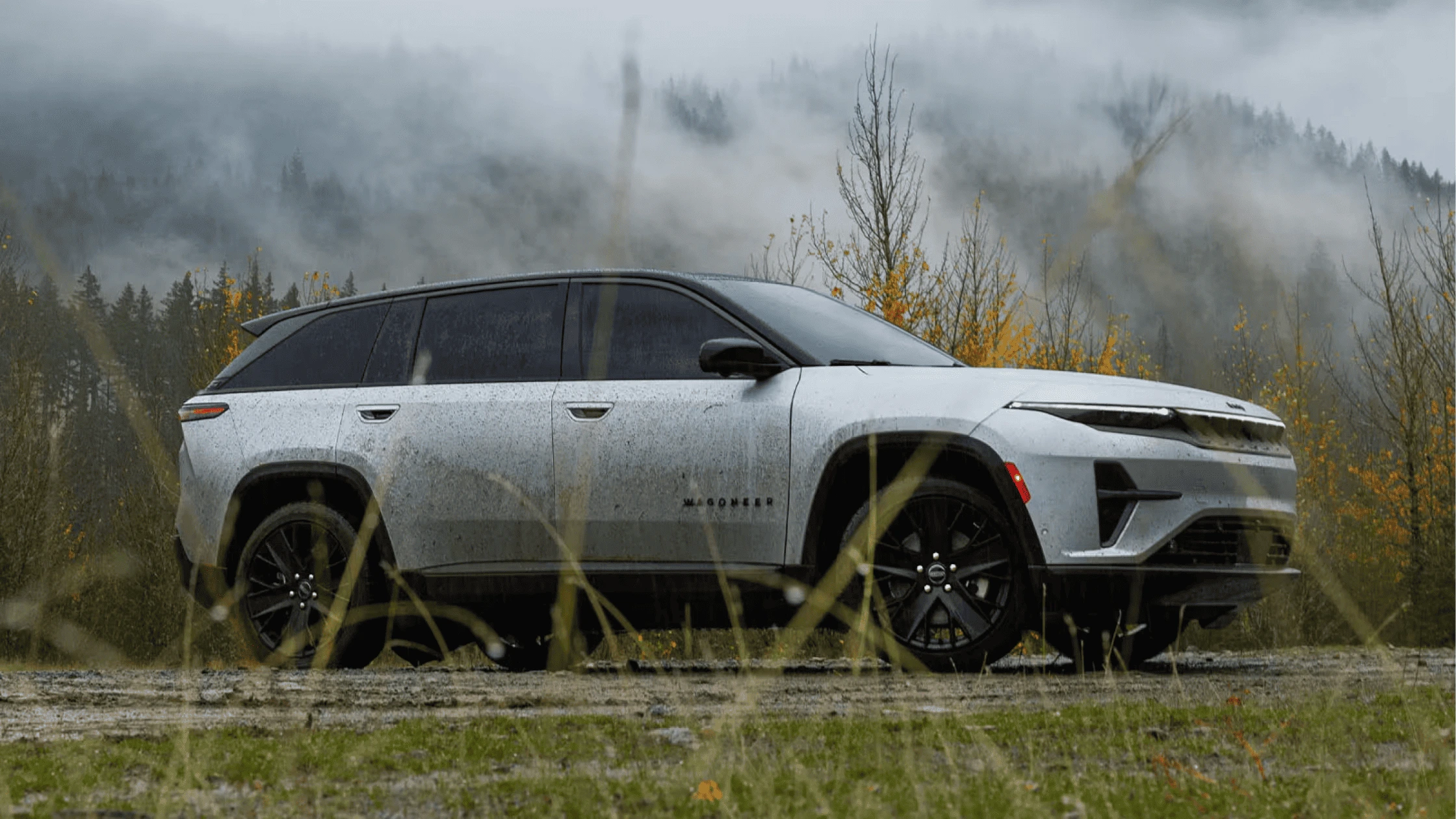 All-electric Jeep® Wagoneer S parked in a rugged outdoor setting, with misty mountains and fall foliage in the background, highlighting its adventure-ready capability and sleek design.
