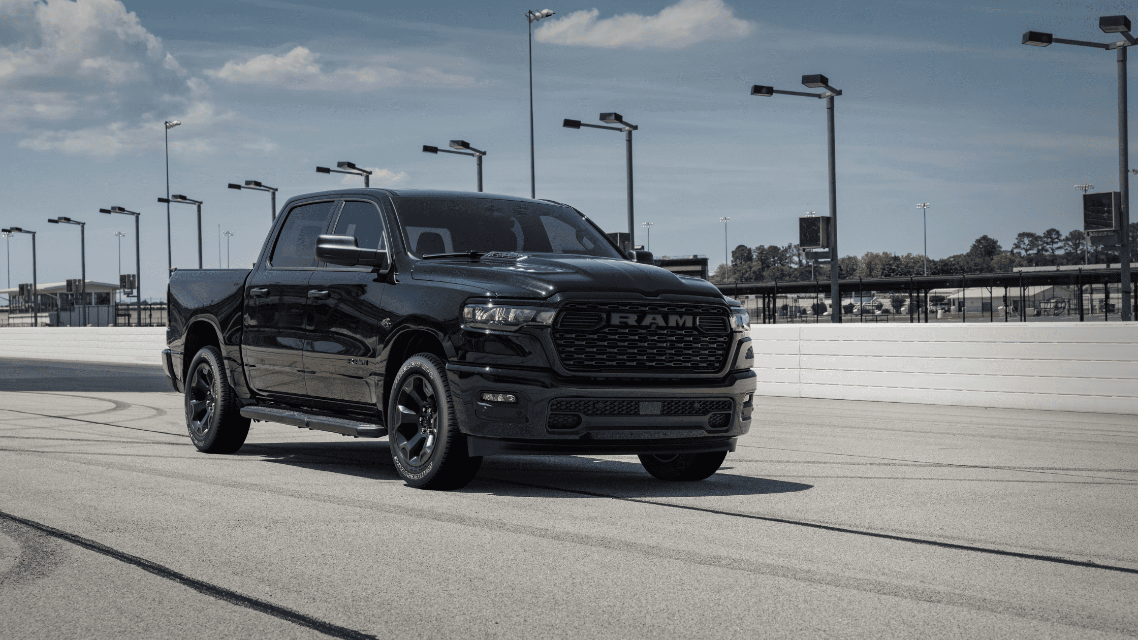 Black 2026 Ram 1500 Express parked on a racetrack under a clear blue sky near Cape Coral, FL, highlighting its bold front grille and wheels.