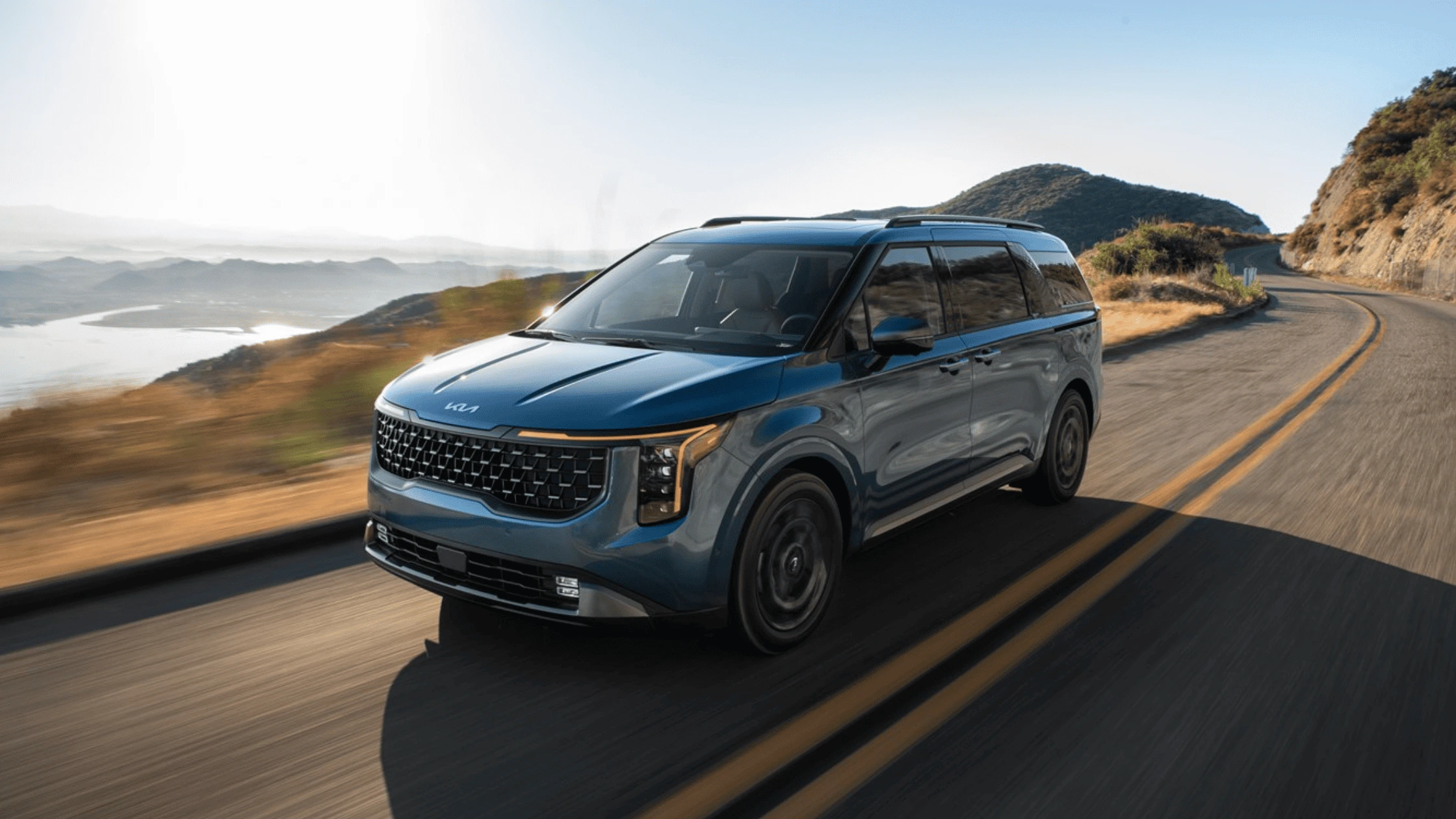 2025 Kia Carnival Hybrid driving on a winding road with scenic mountains in Fort Myers