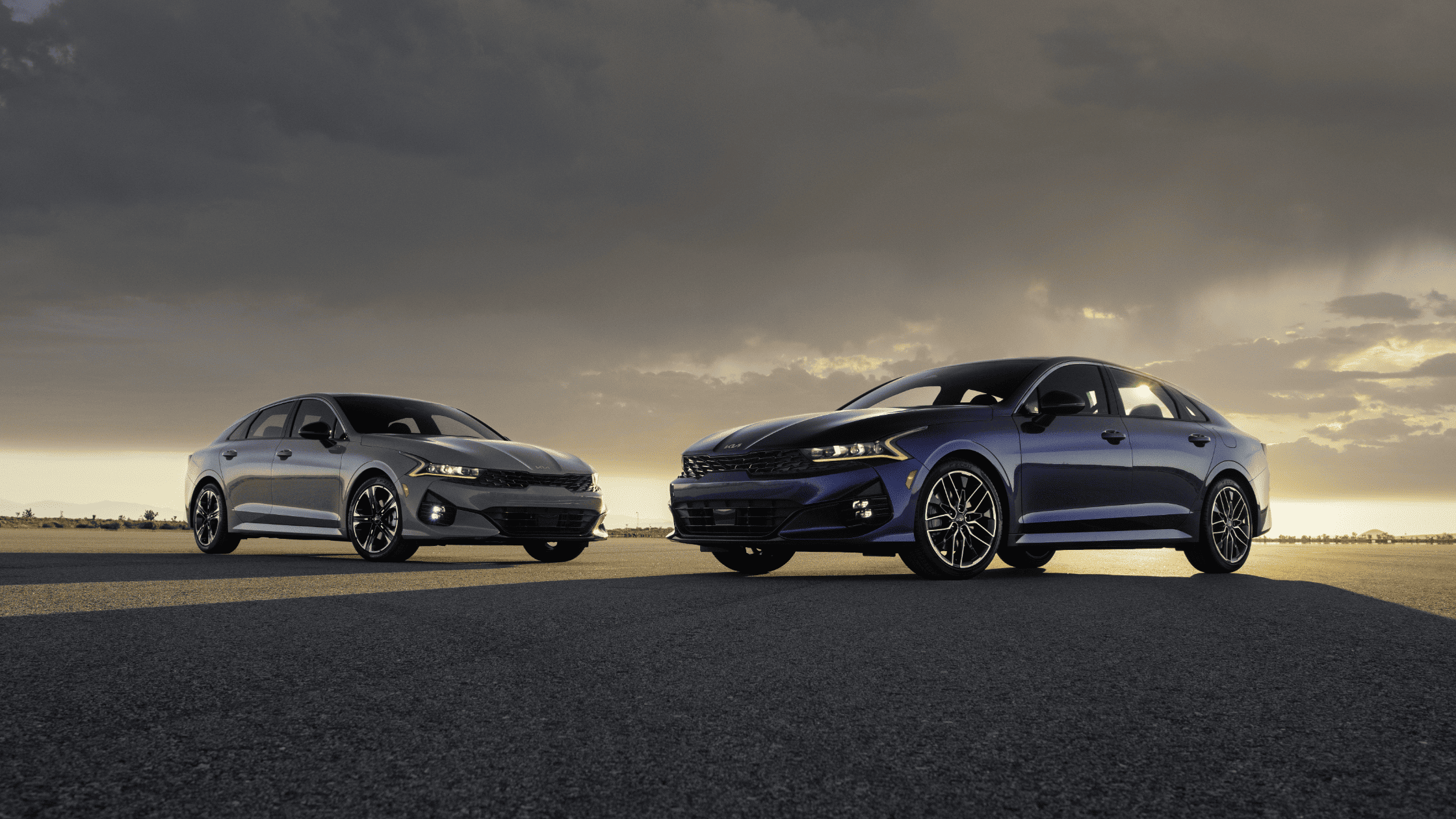 Two 2024 Kia K5 sedans parked on an open road at sunset in Port Charlotte, FL, showcasing the sleek design and performance features that local drivers will love.