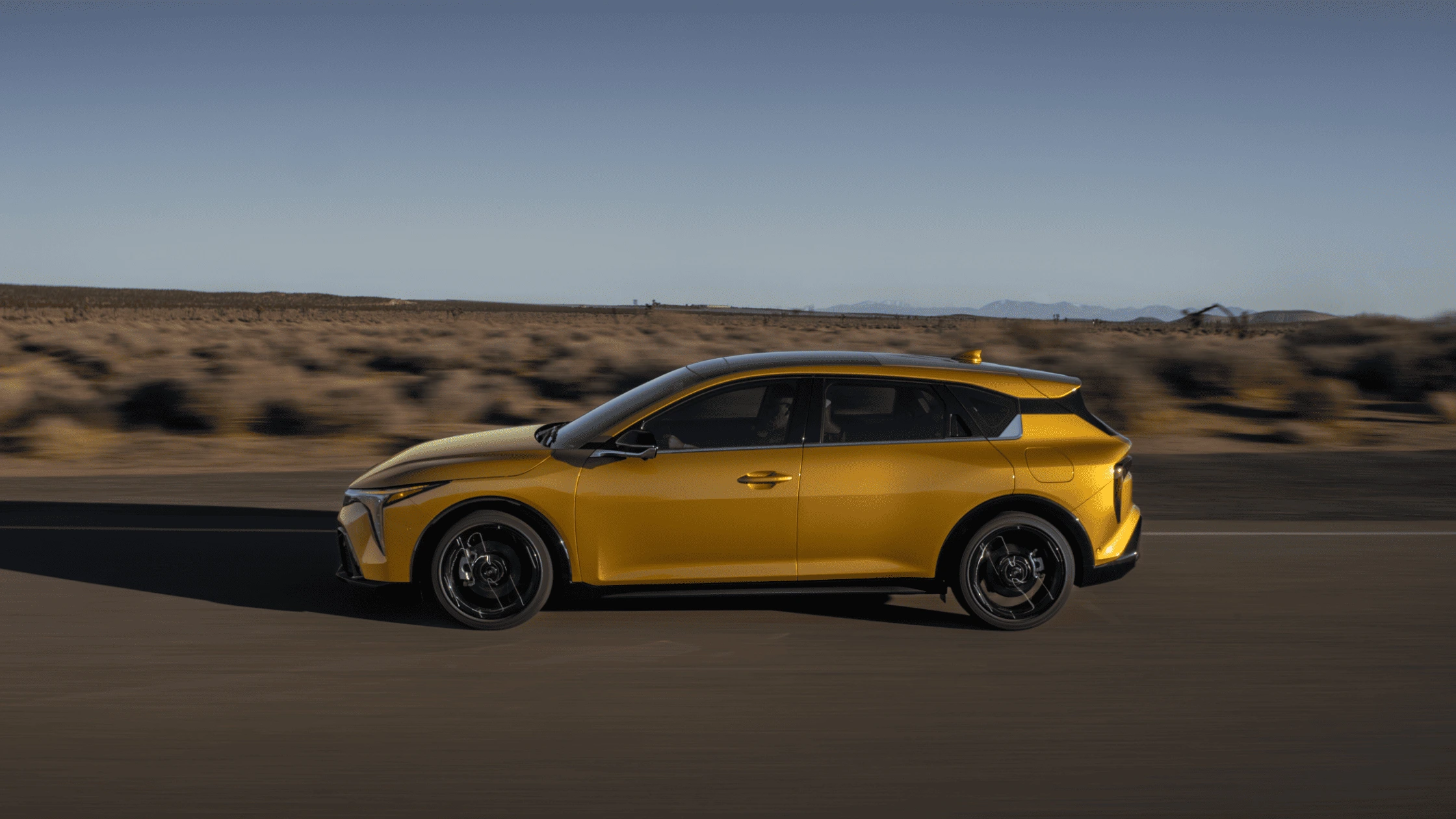 2026 Kia K4 Hatchback in yellow driving through Fort Myers desert road, showcasing bold new design and sporty look.