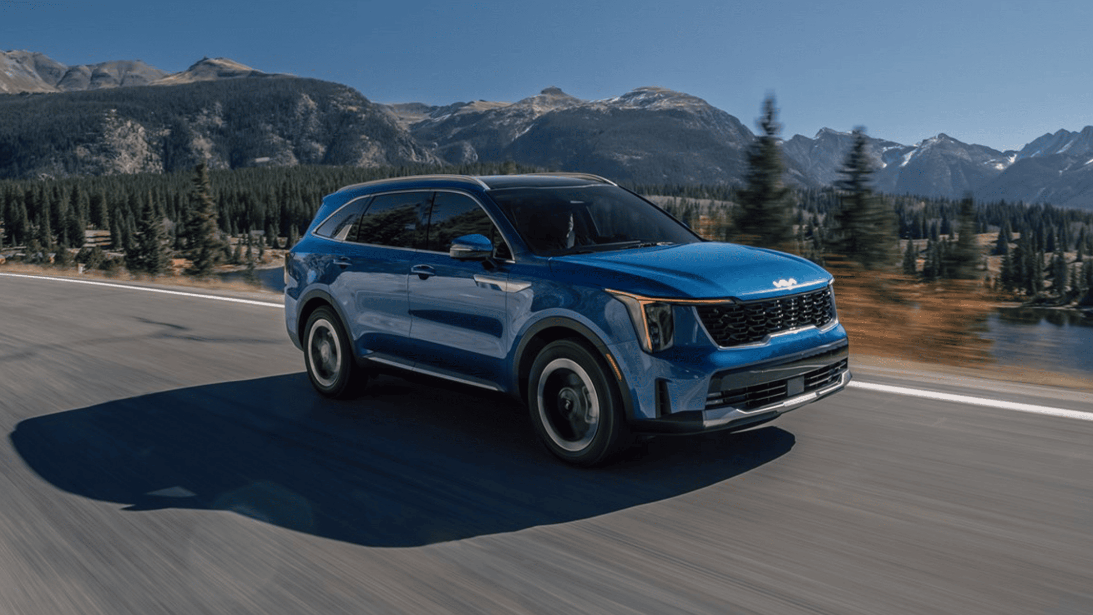 The 2024 Kia Sorento Hybrid in vibrant blue cruising through scenic mountain roads near Port Charlotte, offering eco-friendly performance and modern design.