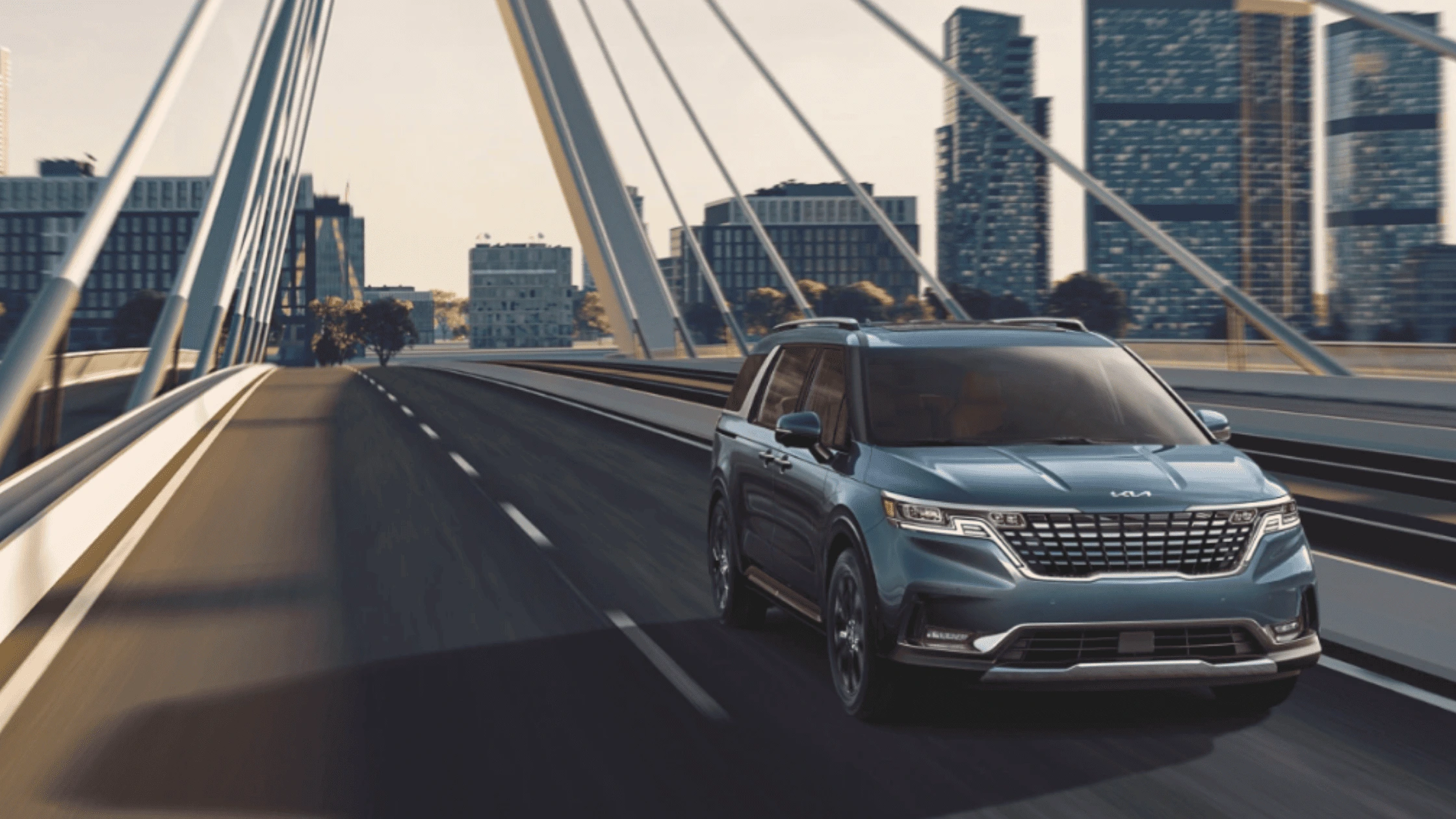 2024 Kia Carnival driving across a modern city bridge, showcasing its sleek design and versatility for Naples families seeking a premium family vehicle.