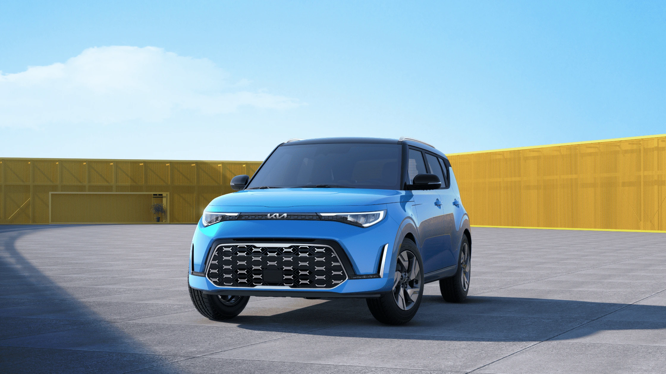 Blue 2025 Kia Soul parked in an open area with a modern yellow fence and blue sky in the background.