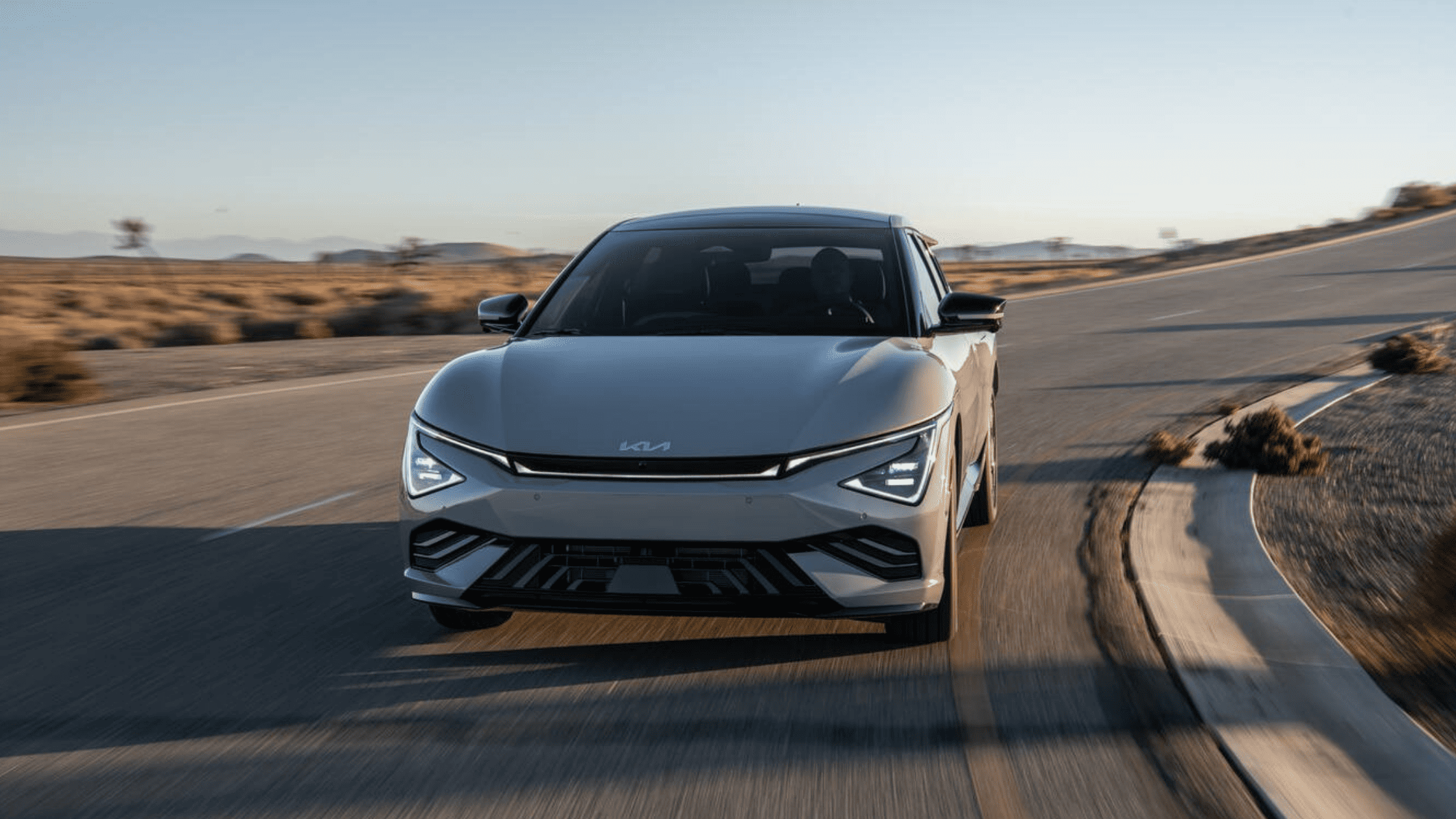 Matte blue 2025 Kia EV6 driving on an open desert road near Cape Coral, FL, showcasing its modern front design and sleek headlights.