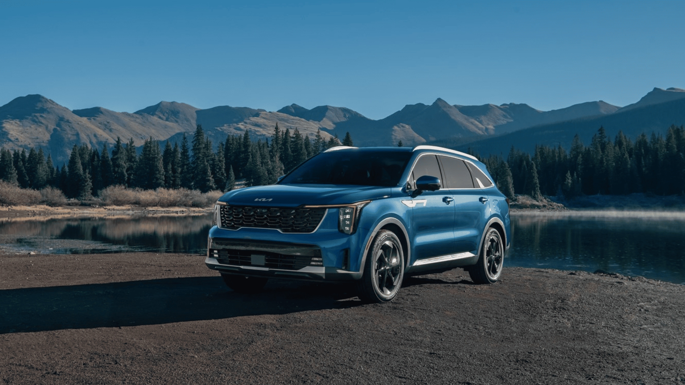 Blue 2025 Kia Sorento Hybrid parked by a serene lake with mountains in the background near Cape Coral, FL.