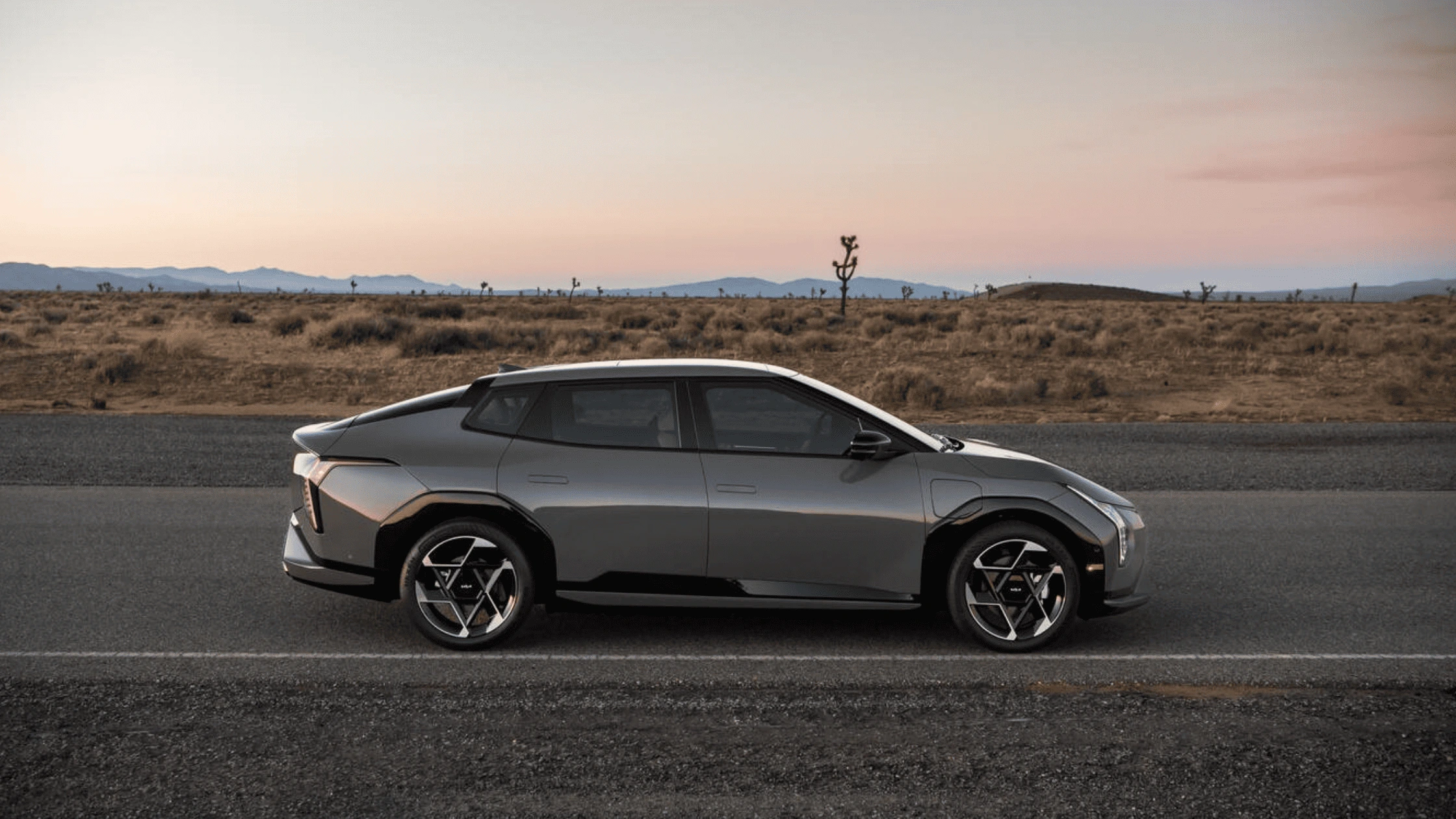 Side view of a 2026 Kia EV4 electric SUV parked along the highway near Fort Myers, with sunset desert background.
