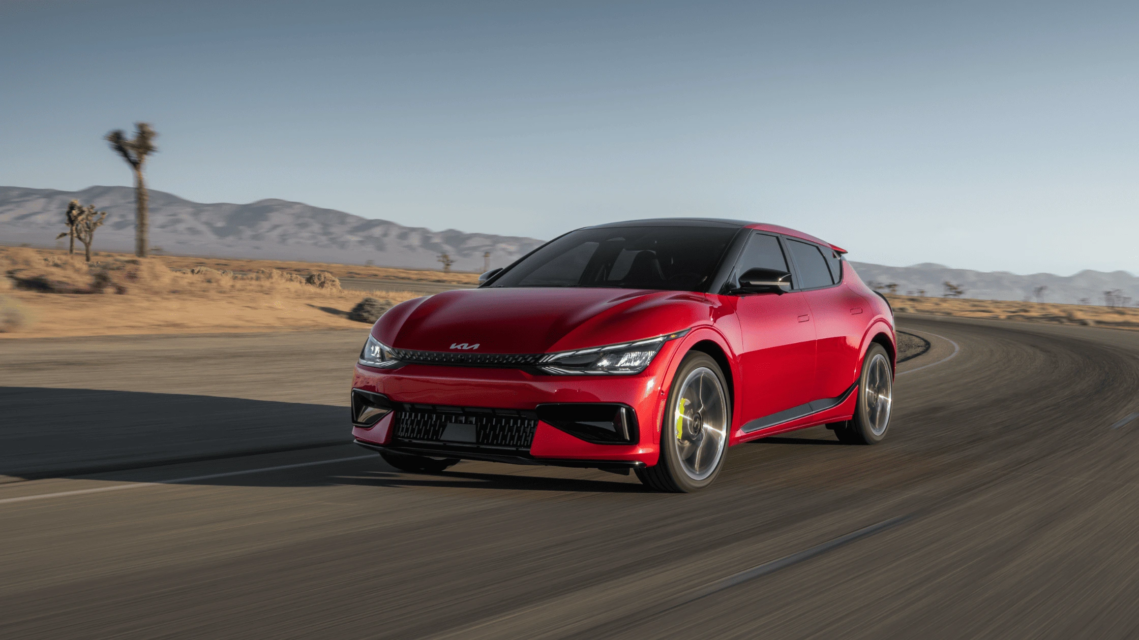 2024 Kia EV6 in vibrant red driving through a desert landscape, showcasing its sleek electric design and performance for Naples, FL residents.