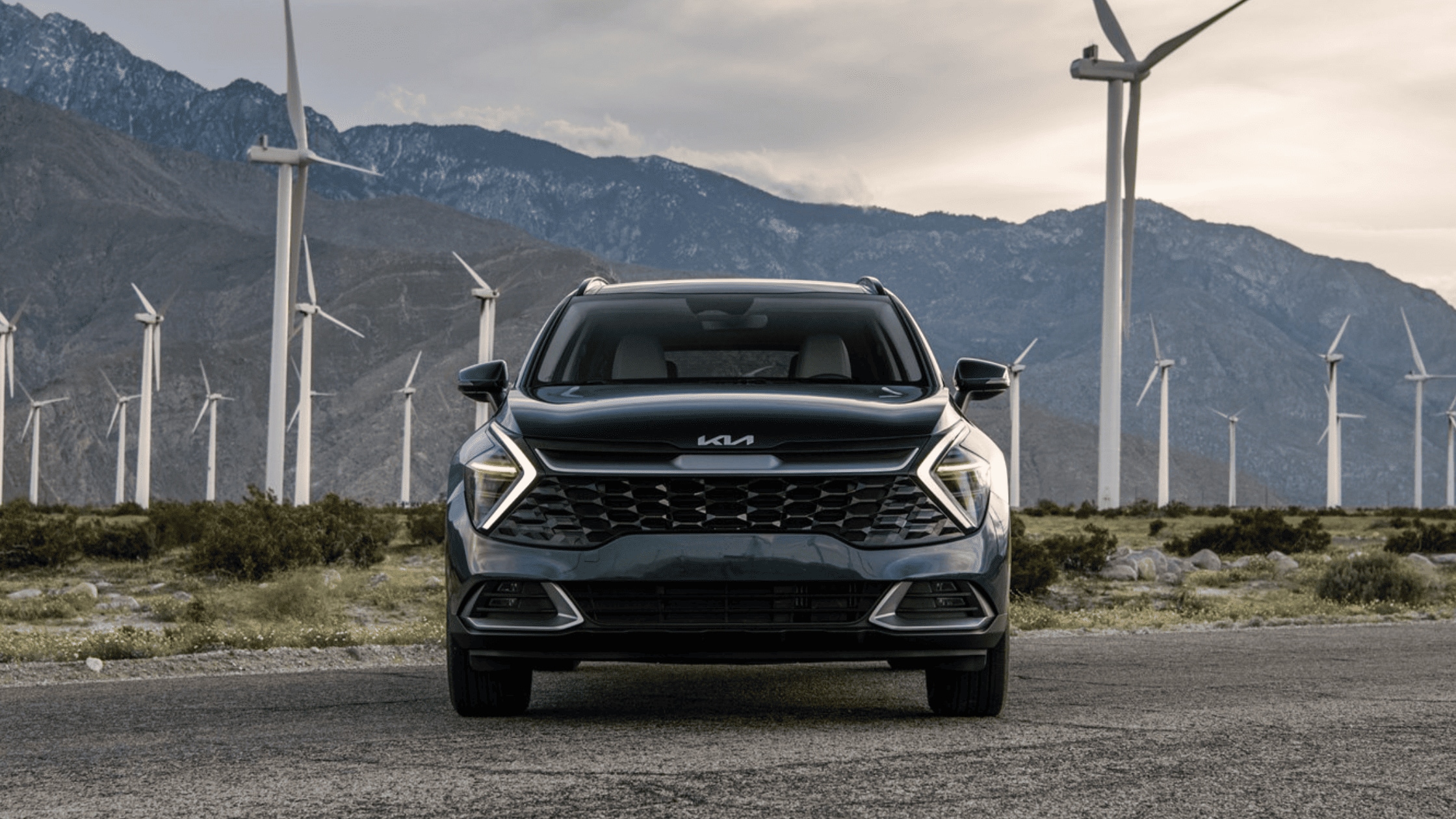 2024 Kia Sportage Hybrid parked in front of wind turbines, highlighting its eco-friendly hybrid technology and modern design, a favorite SUV in Port Charlotte.