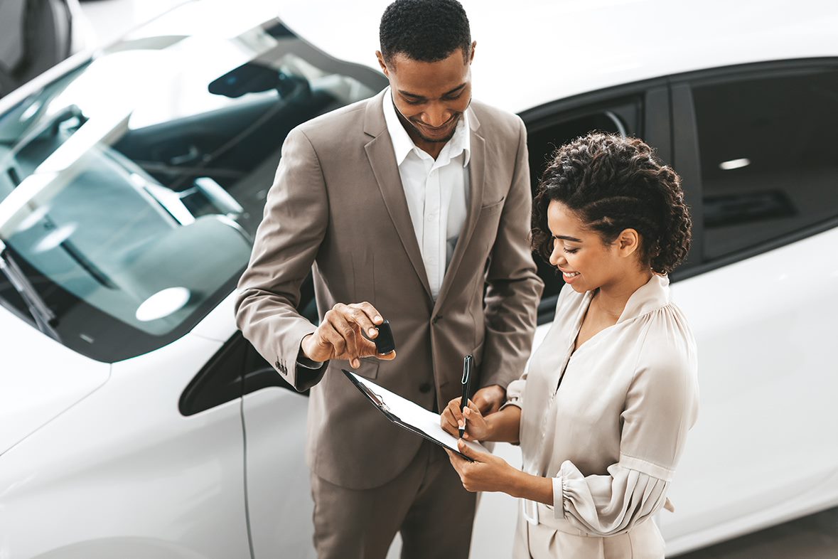 dealer and customer finishing paperwork next to a white car