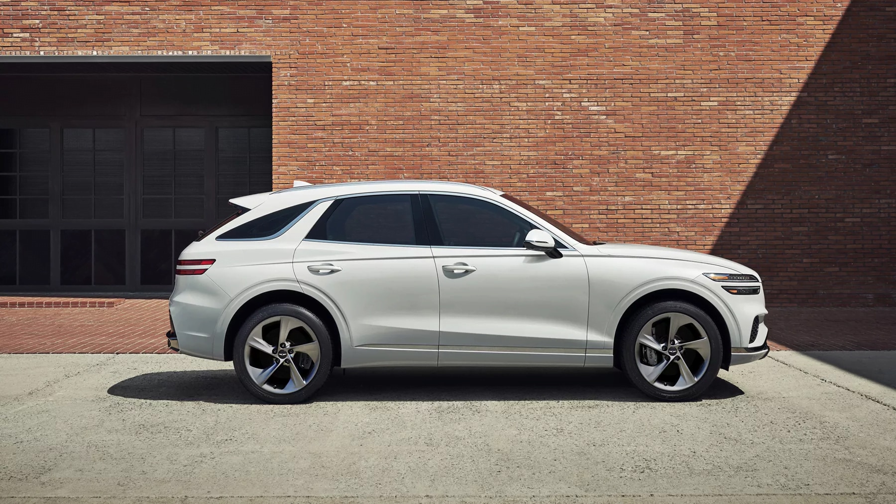 White 2026 Genesis GV70 SUV parked beside a modern brick building.