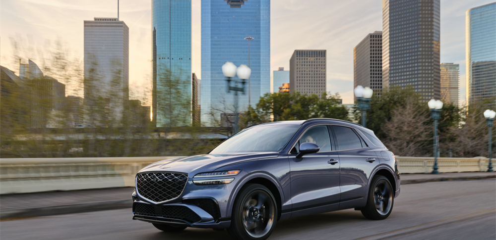 Genesis GV70 driving through a downtown city skyline at sunset.