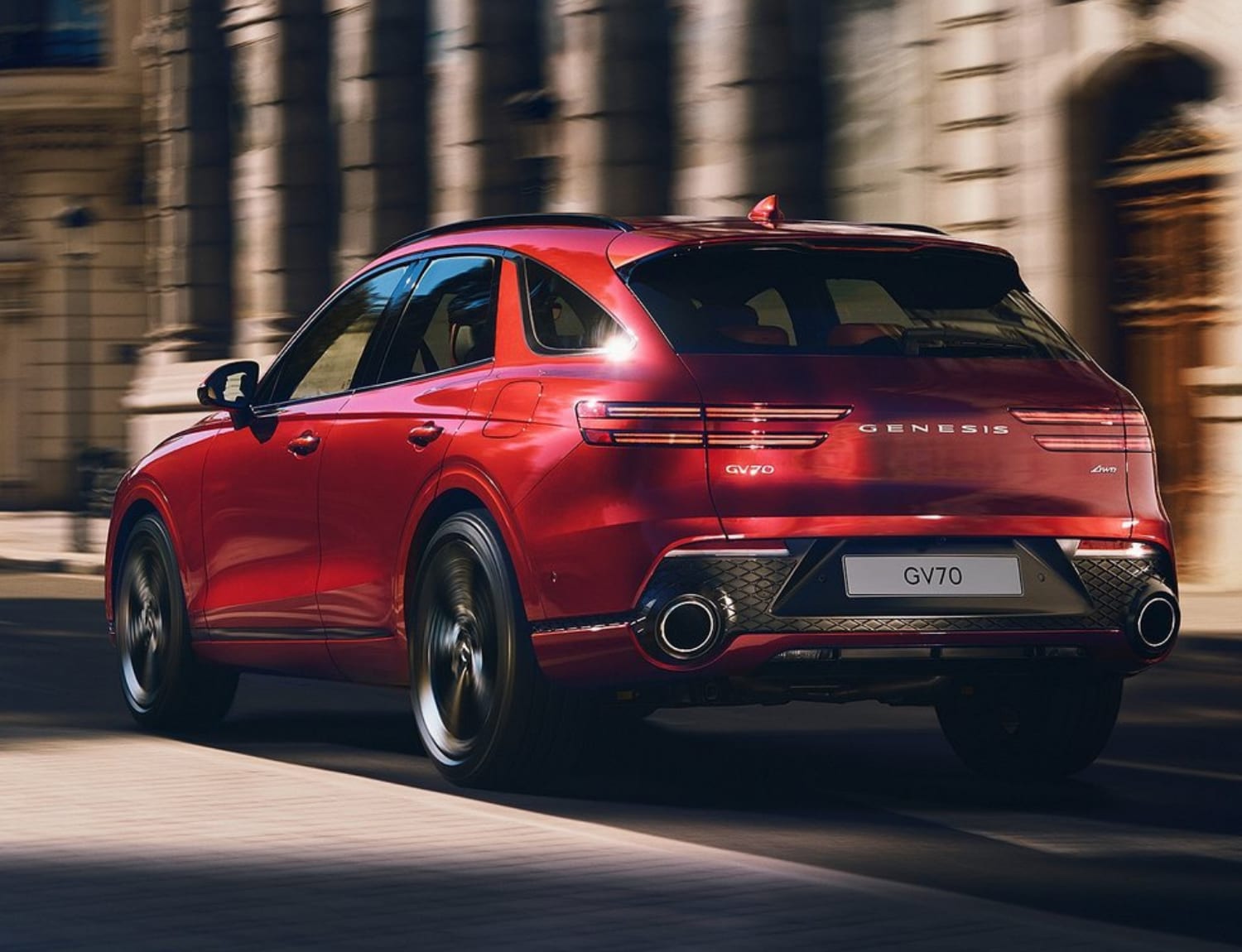 All-New 2022 Genesis GV70 SUV Powertrain Specs.png Rear exterior view of a 2022 Genesis GV70 SUV driving fast away from the camera lens showing off the powerful dual exhuast system