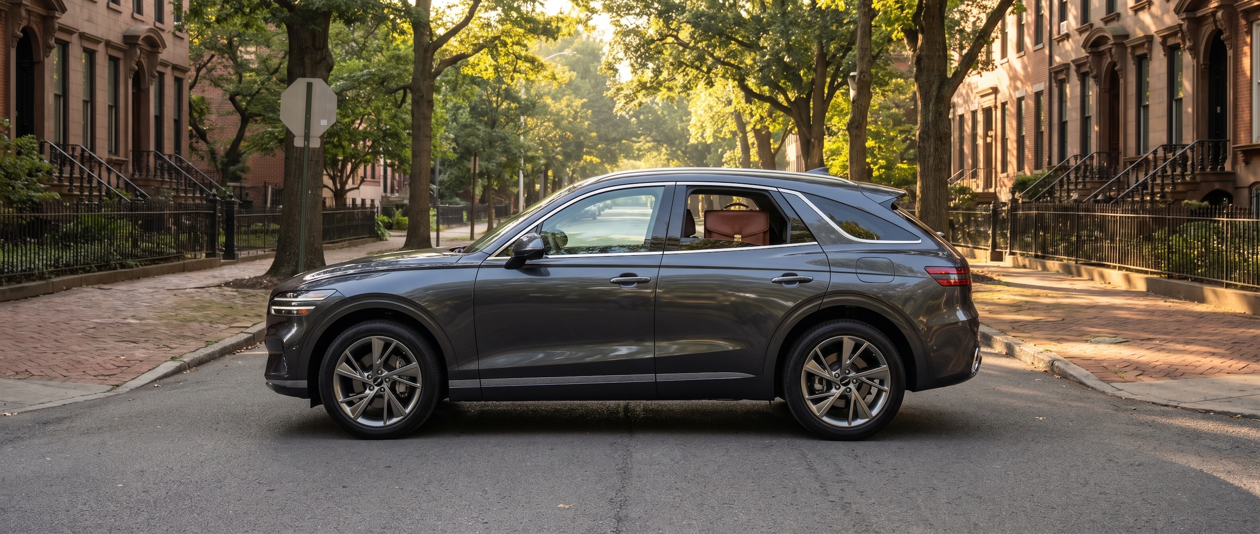 A 2026 Genesis GV70 in a refined dark finish parked near a tree-lined Nashville campus street in late summer, with a briefcase visible through the rear window, natural morning light, professional urban setting