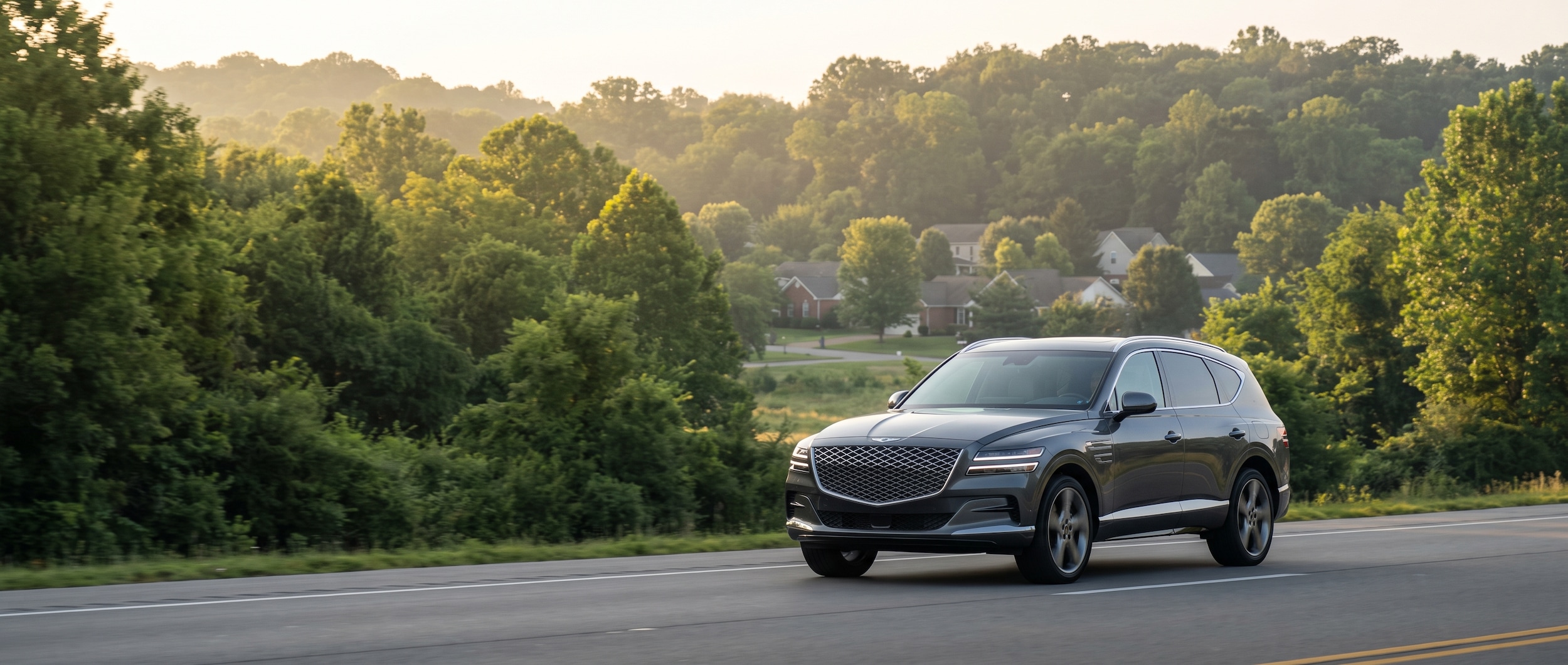 A 2026 Genesis GV80 in white or dark finish driving on an open Tennessee highway, morning light, lush green tree line visible, family-oriented suburban setting suggesting South Nashville or Antioch corridor