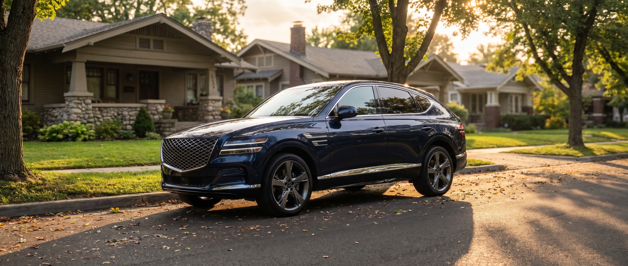A 2026 Genesis GV80 Coupe in dark navy or black, parked on a tree-lined residential street evocative of 12 South Nashville -- craftsman bungalows in the soft background, warm summer afternoon light, the coupe's raked roofline prominent from a low three-quarter front angle.