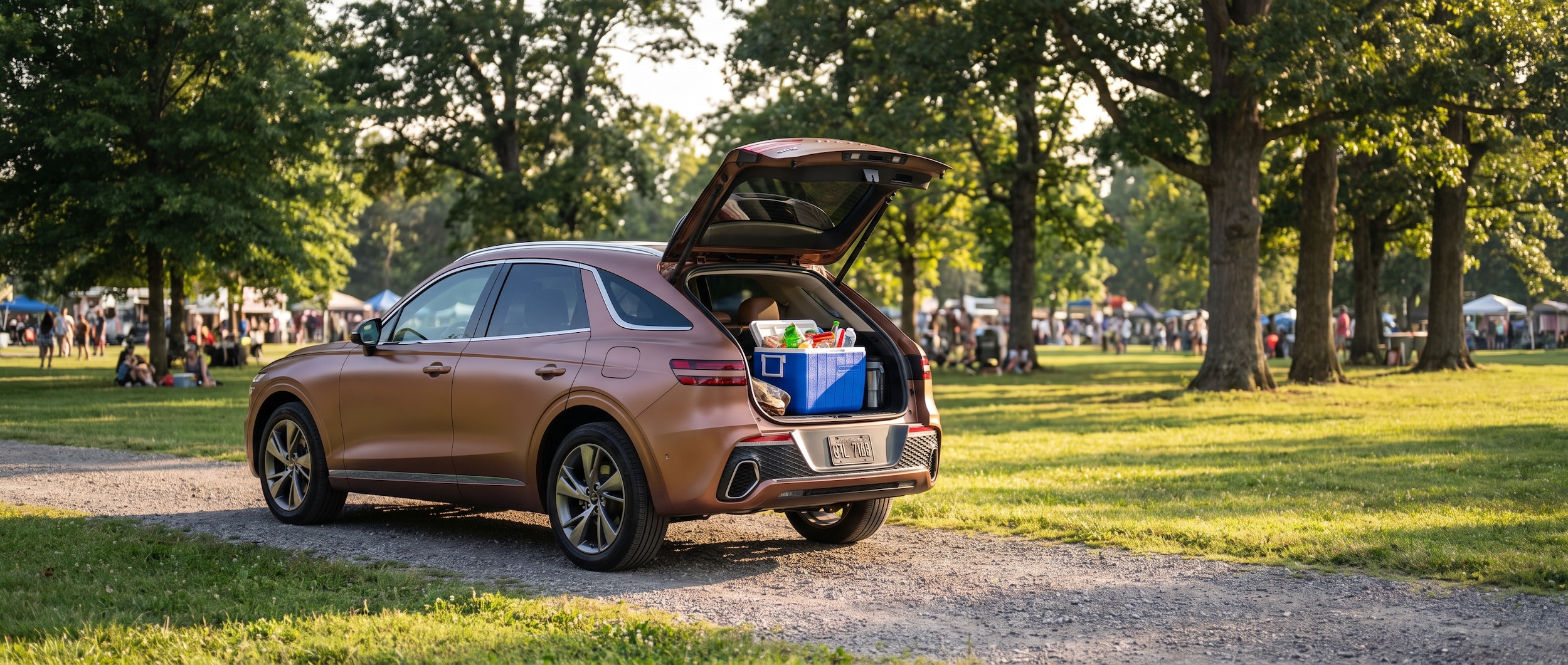 A 2026 Genesis GV70 in a warm metallic finish parked near a tree-lined Nashville park, tailgate open and a packed cooler visible, late-afternoon summer light casting long shadows, green festival grounds in the background