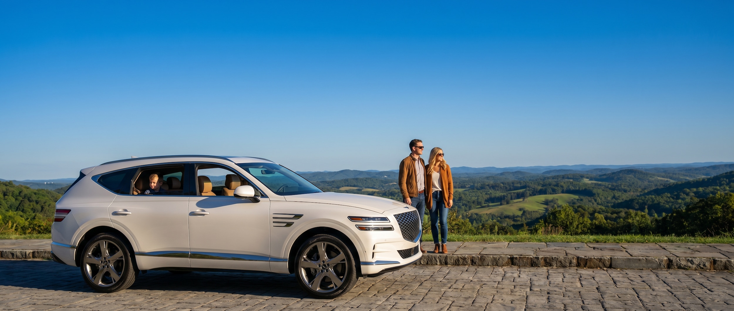 A refined pearl-white luxury SUV parked in front of a scenic overlook with rolling Tennessee hills and a clear blue sky in the background, conveying sophistication and family confidence.
