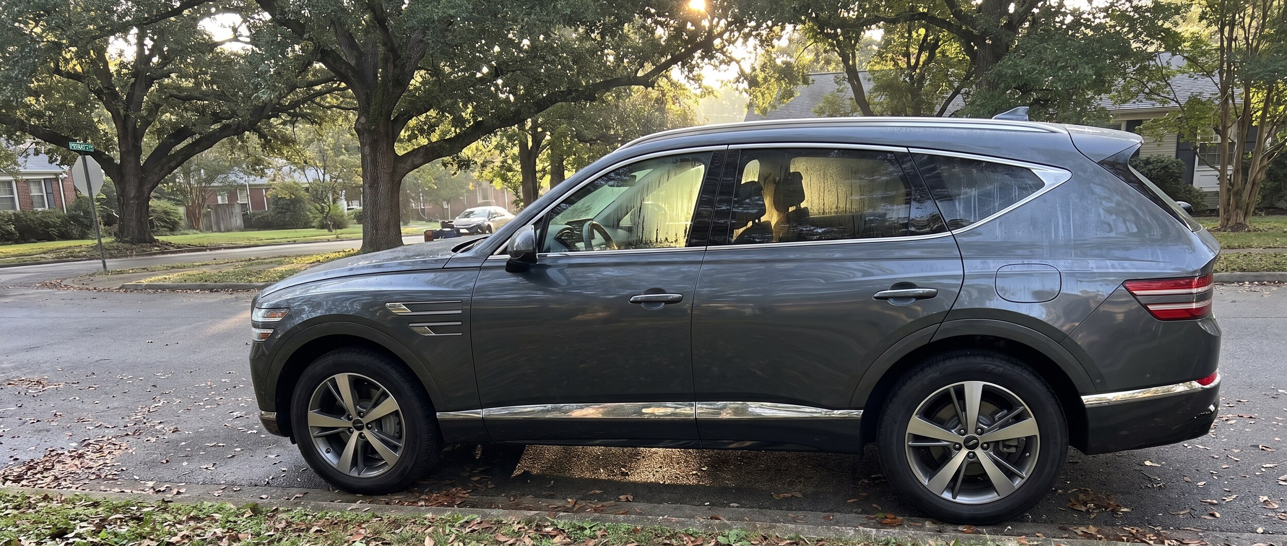 A sleek Genesis GV80 parked in a tree-lined Nashville neighborhood on a warm summer morning, with the cabin glowing softly as if recently climate-controlled, condensation gently clearing from the windows.