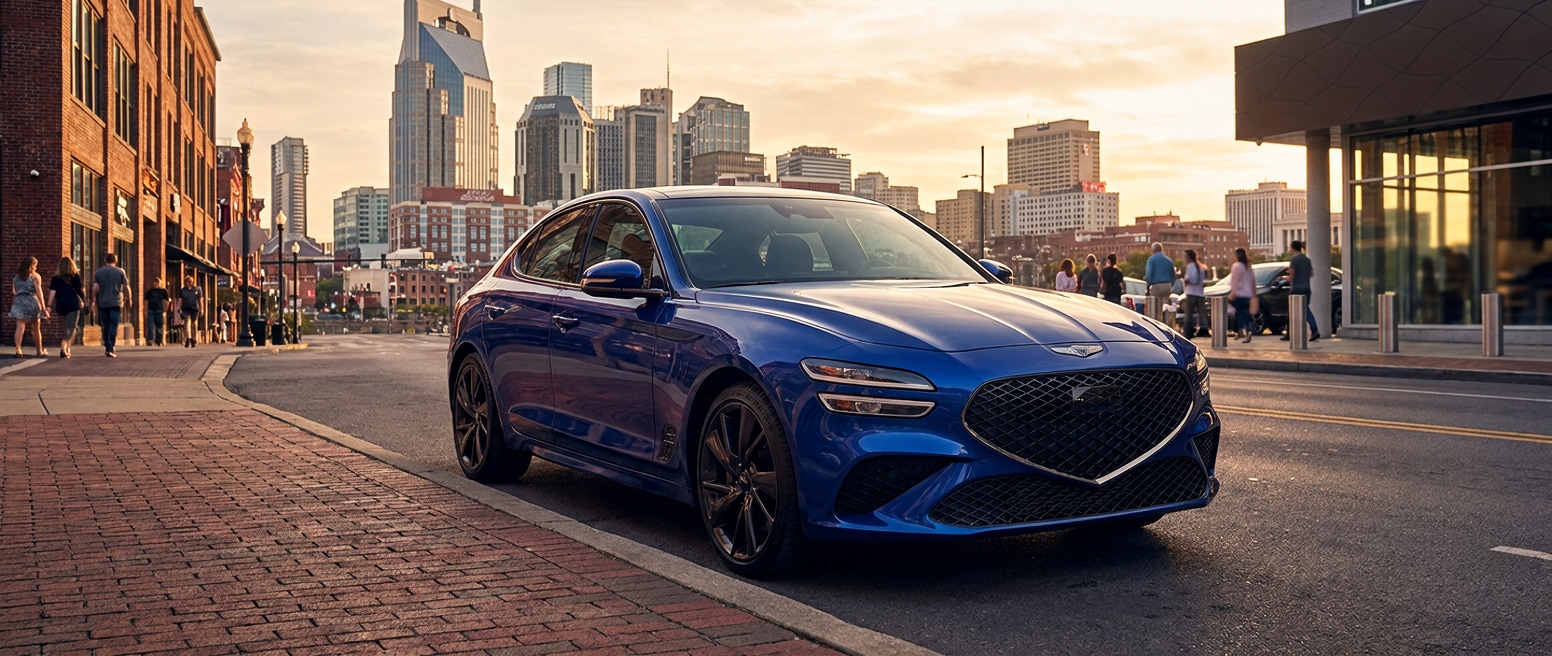 A 2026 Genesis G70 in deep metallic paint parked on a Nashville city street with the downtown skyline visible in warm late-afternoon light, conveying a refined urban sport sedan character