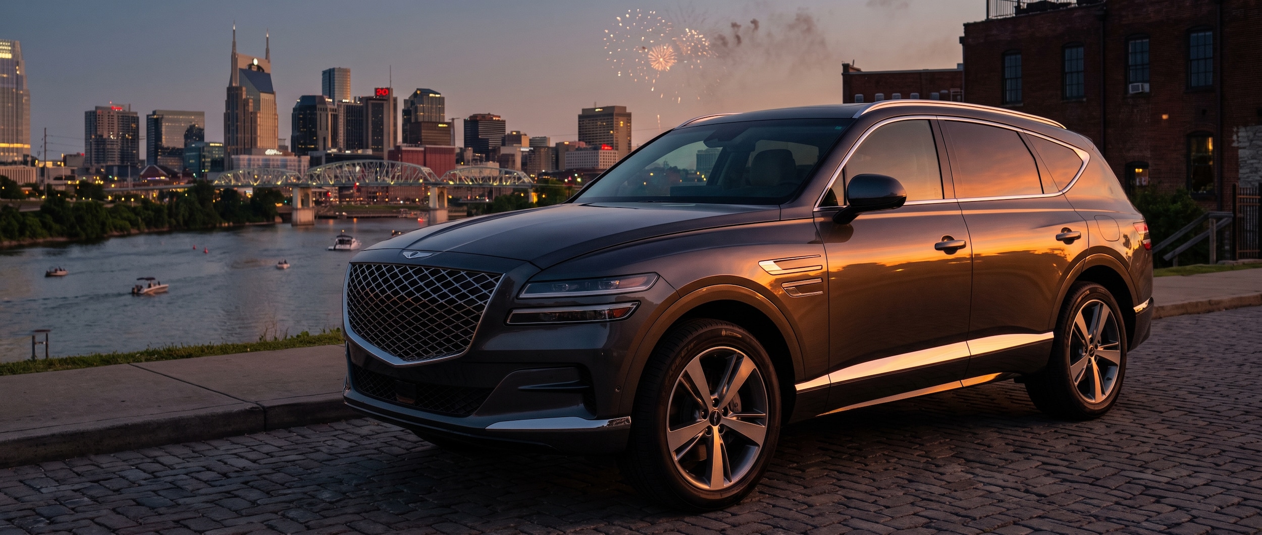 A polished Genesis GV80 in a dark metallic finish parked on a quiet Nashville side street at dusk, Cumberland River and glowing downtown skyline visible in the background, warm summer evening light, fireworks faintly visible in the sky above.