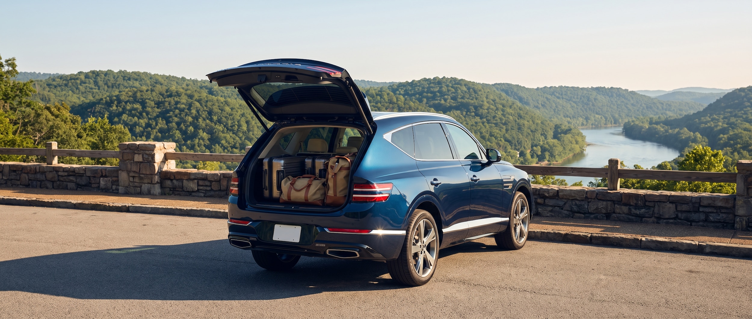 A 2026 Genesis GV80 SUV in a rich dark finish, rear liftgate open to reveal a neatly loaded cargo area with rolling suitcases and duffel bags, parked at a Tennessee highway overlook on a sunny summer morning with tree-covered hills in the background