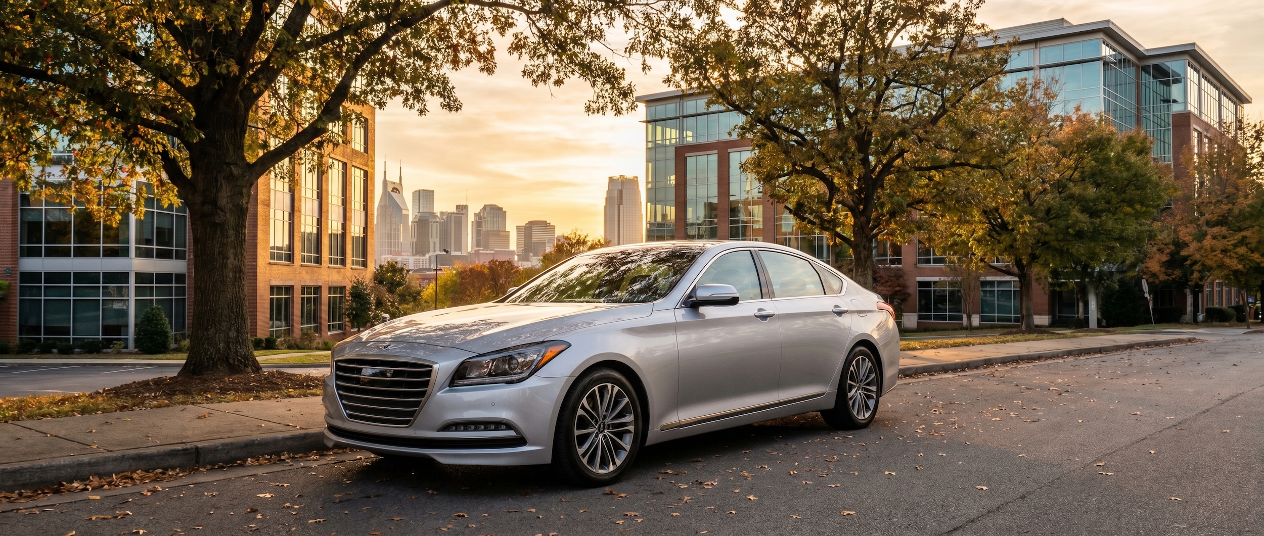 A sleek silver Genesis G80 parked on a tree-lined Nashville street near a modern office building, late afternoon light reflecting off the hood, downtown skyline visible in the background.