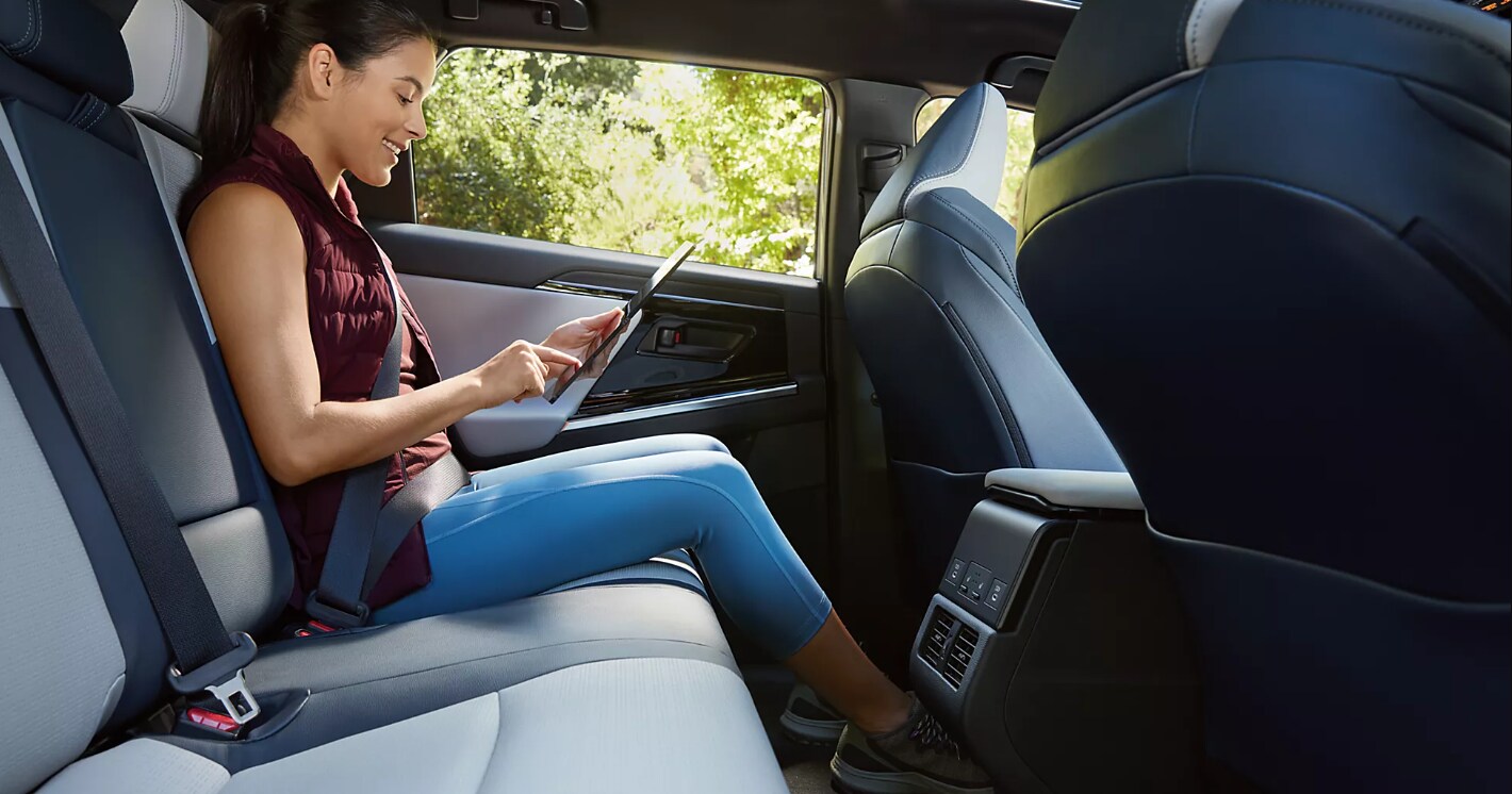 A woman sits in the backseat of a 2023 Subaru Solterra while using a laptop
