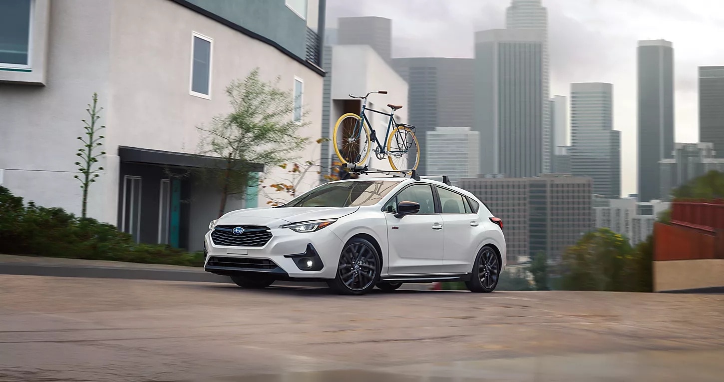 2025%204Runner%20Price%20and%20Trim.png White 2025 Subaru Impreza in the middle of a city with a bike mounted on top.