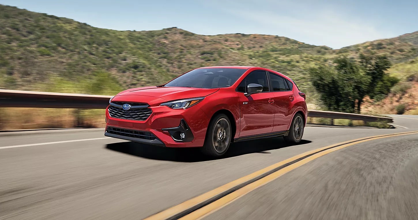 Red 2025 Subaru Impreza driving down a desert road.