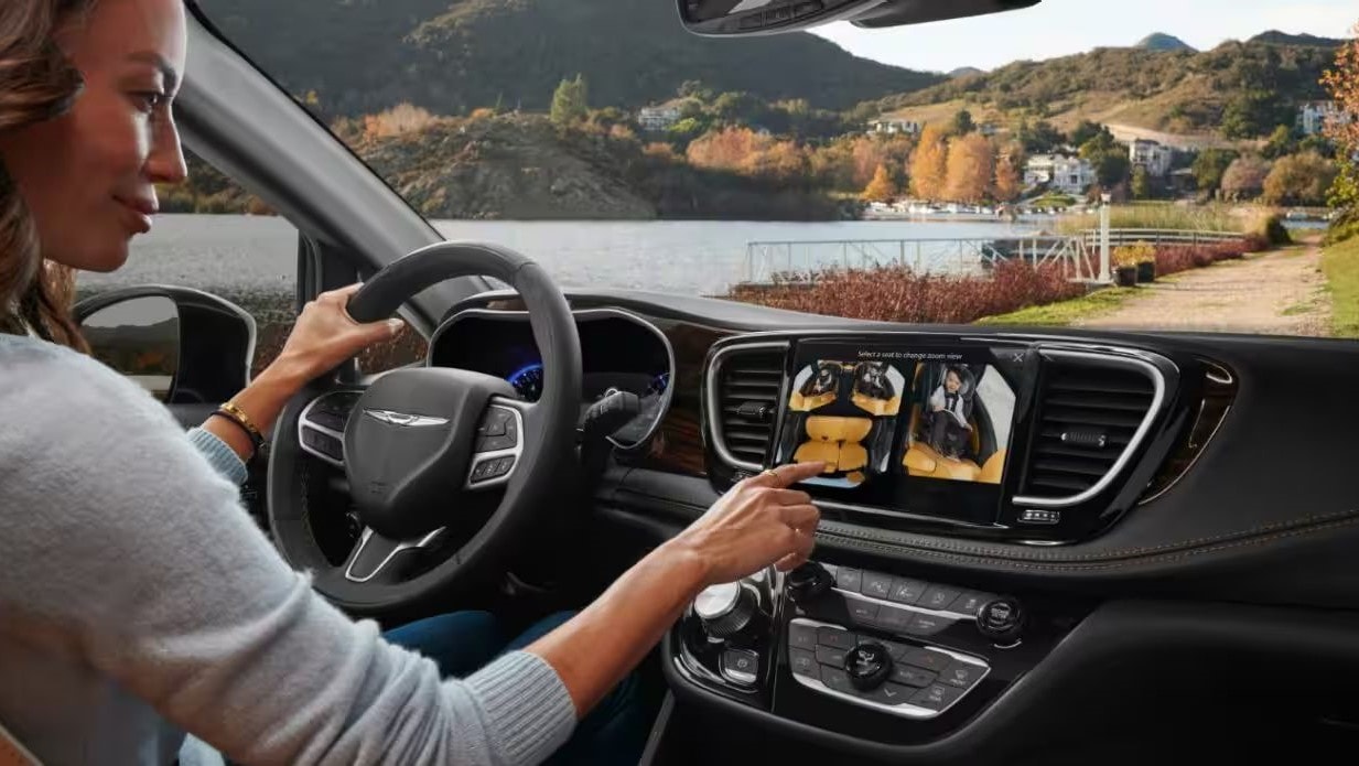 Interior shot of the 2023 Chrysler Pacifica with a woman behind the steering wheel, her left hand is on the steering wheel, while her right hand is using the touchscreen controls on the dashboard.