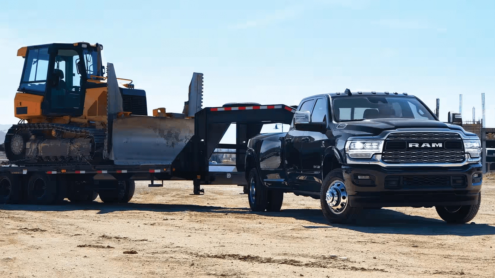 Exterior shot of a black Ram 3500 towing a bulldozer at a worksite.