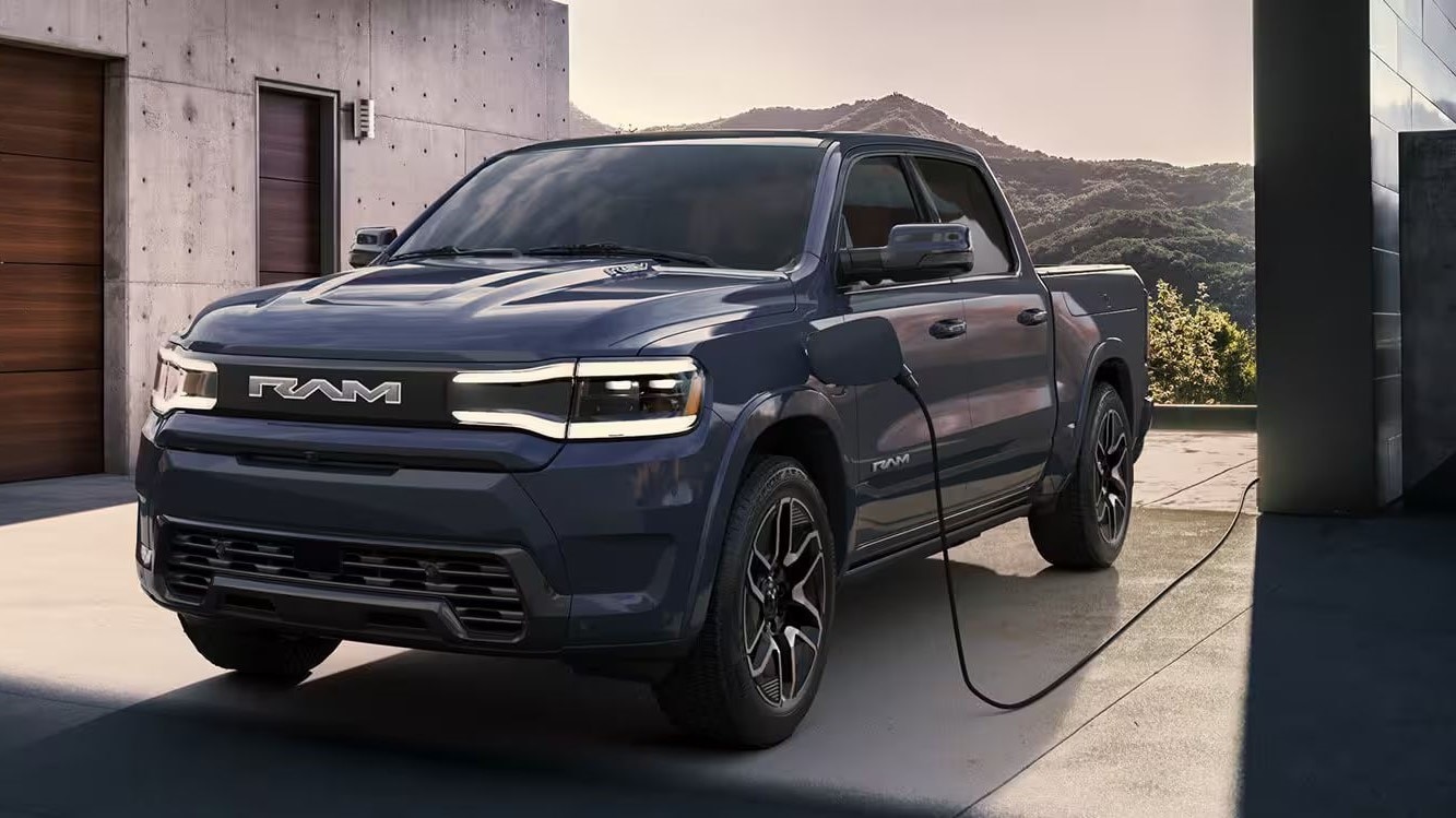 RAM 1500 REV plugged in and charging outside an industrial style home. Mountainous terrain can be seen in the background.