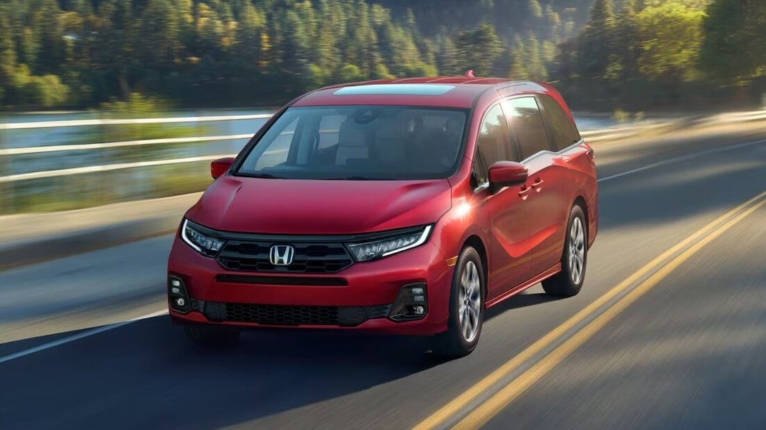 A red Honda Odyssey driving down a road in a forest, the scene behind it blurring.