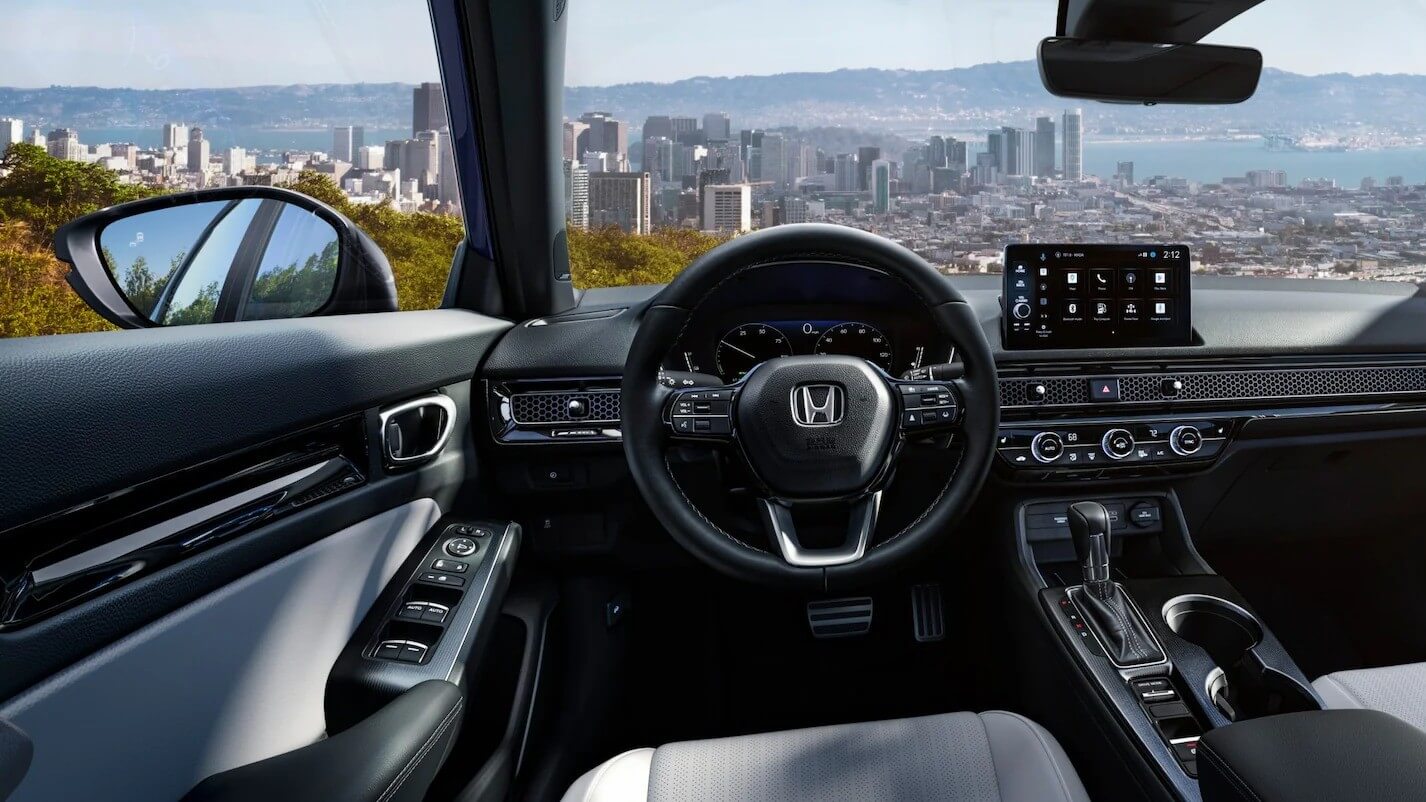  A picture from the interior of a Honda Civic looking out through the windshield at a city.