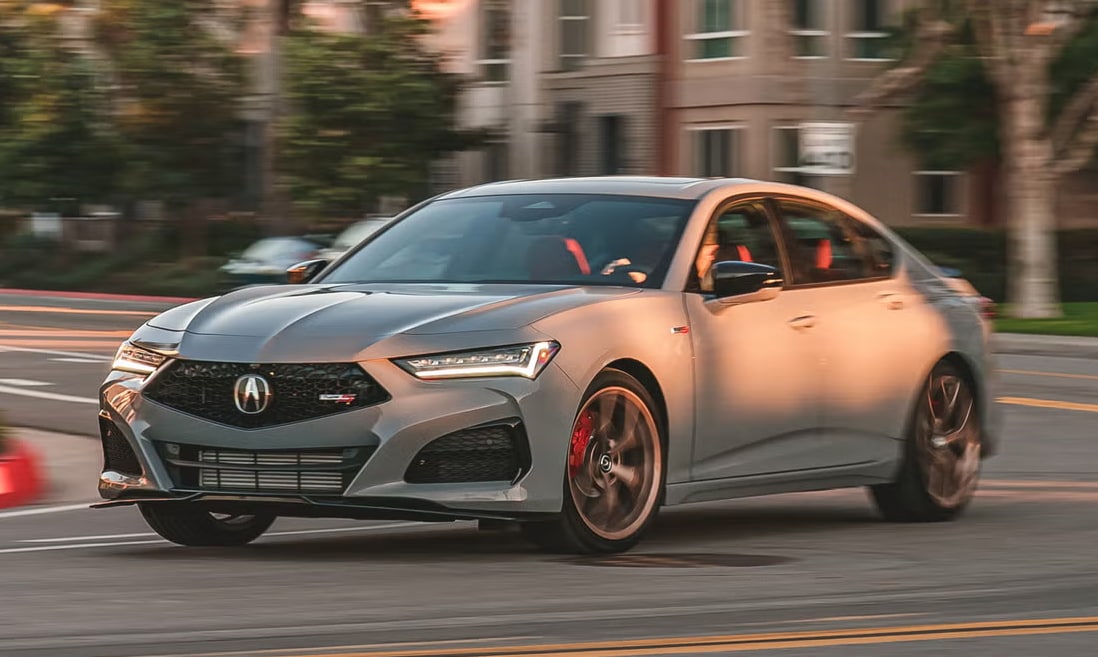 Silver Acura sedan driving through a city street near Acura Goodson dealership, showcasing sleek design and performance.