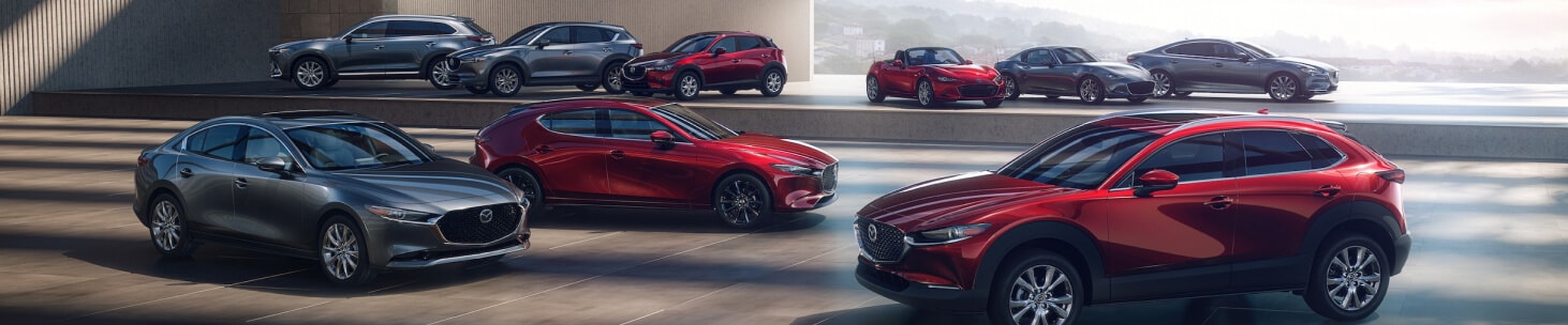 Wide angle showing the entire 2026 Mazda lineup parked dramatically in a modern, well lit parking structure.