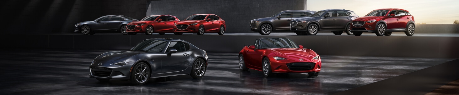Wide angle showing the entire 2020 Mazda lineup parked side-by-side in a dark, hazy parking structure.