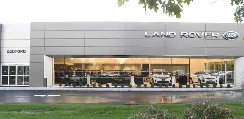 Front exterior view of Land Rover Bedford dealership showcasing white and black SUVs through a glass showroom window.