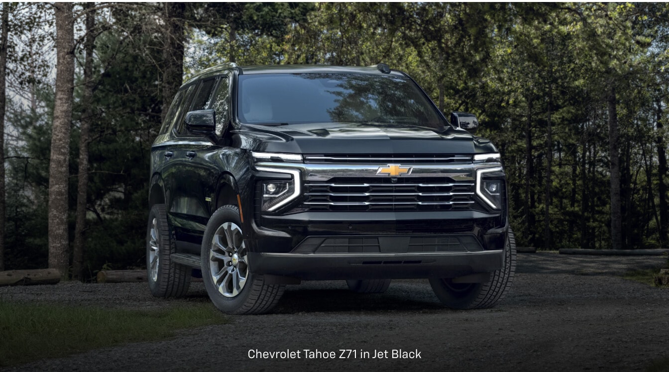 Chevrolet Tahoe parks on a gravel trail surrounded by dense green forest trees.