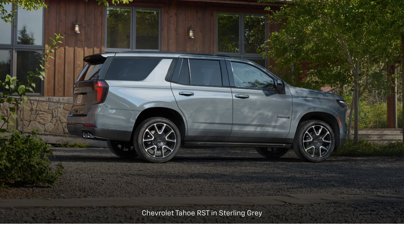 Chevrolet Tahoe parks on a gravel driveway in front of a modern wooden cabin.