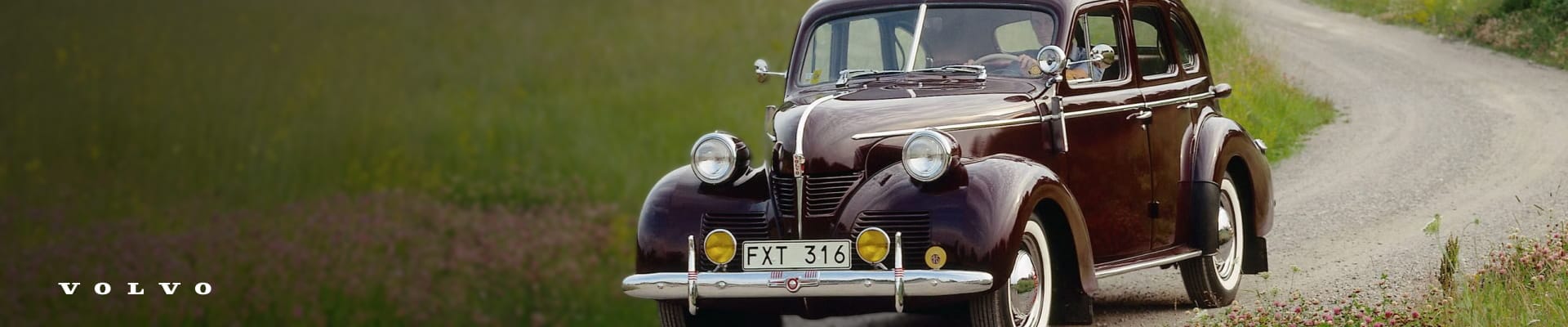 Vintage Volvo sedan driving along a country road surrounded by green field.