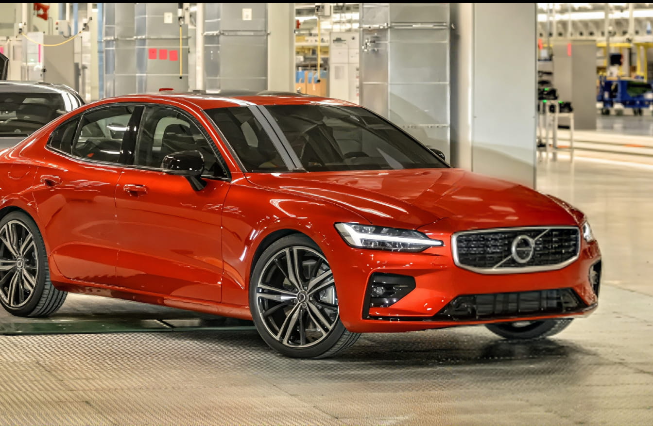 Red Volvo sedan shown from a front three-quarter angle inside a vehicle manufacturing facility.
