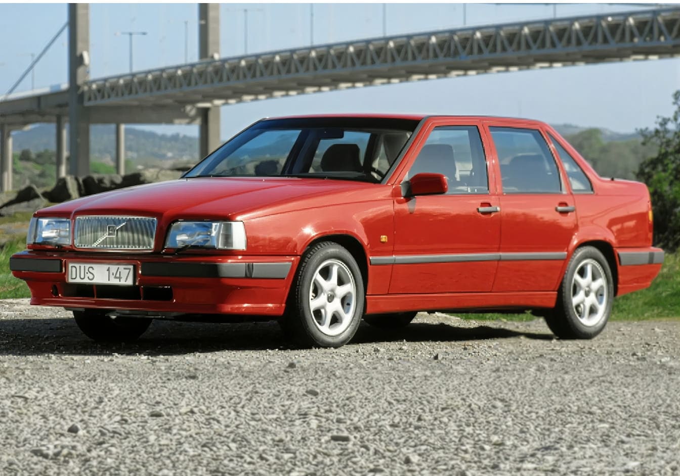 Red Volvo sedan parked near a large bridge, shown from a front three-quarter angle.