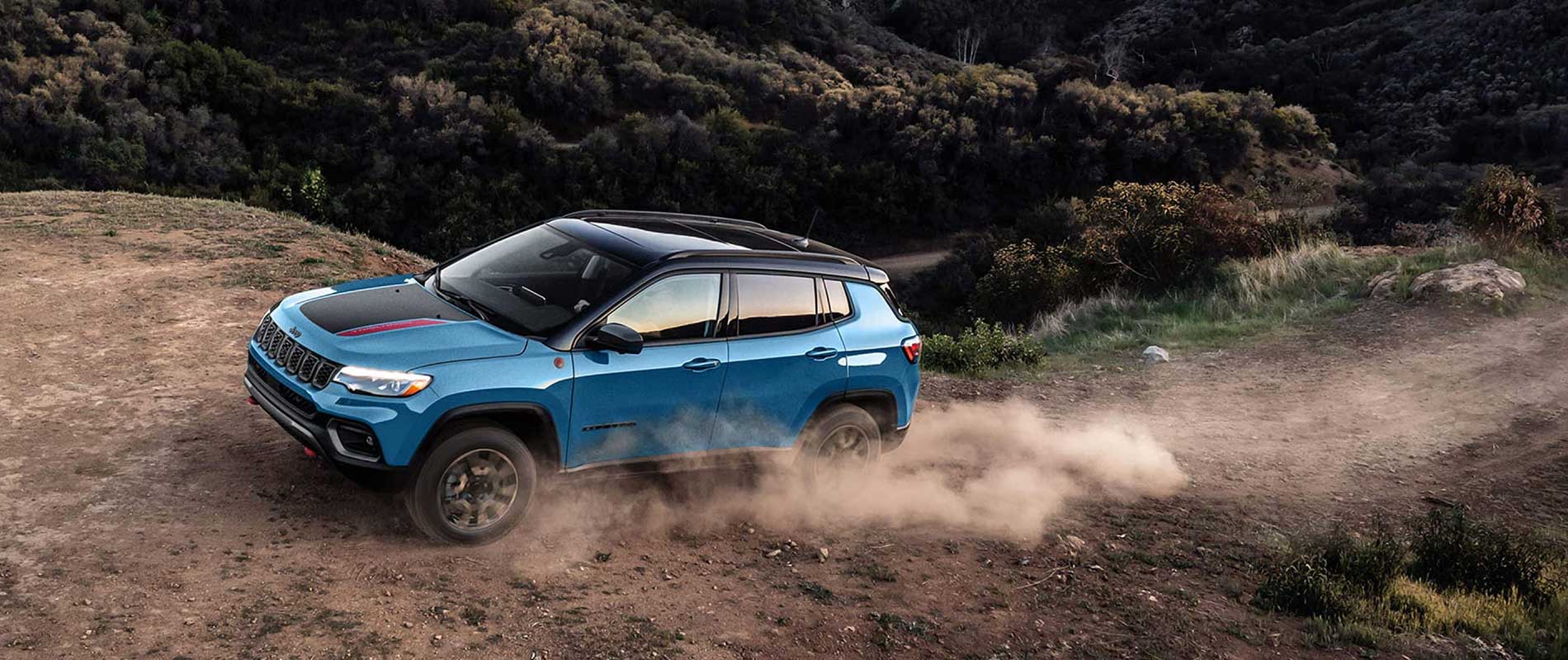 A blue Jeep Compass driving up a dirt hill.