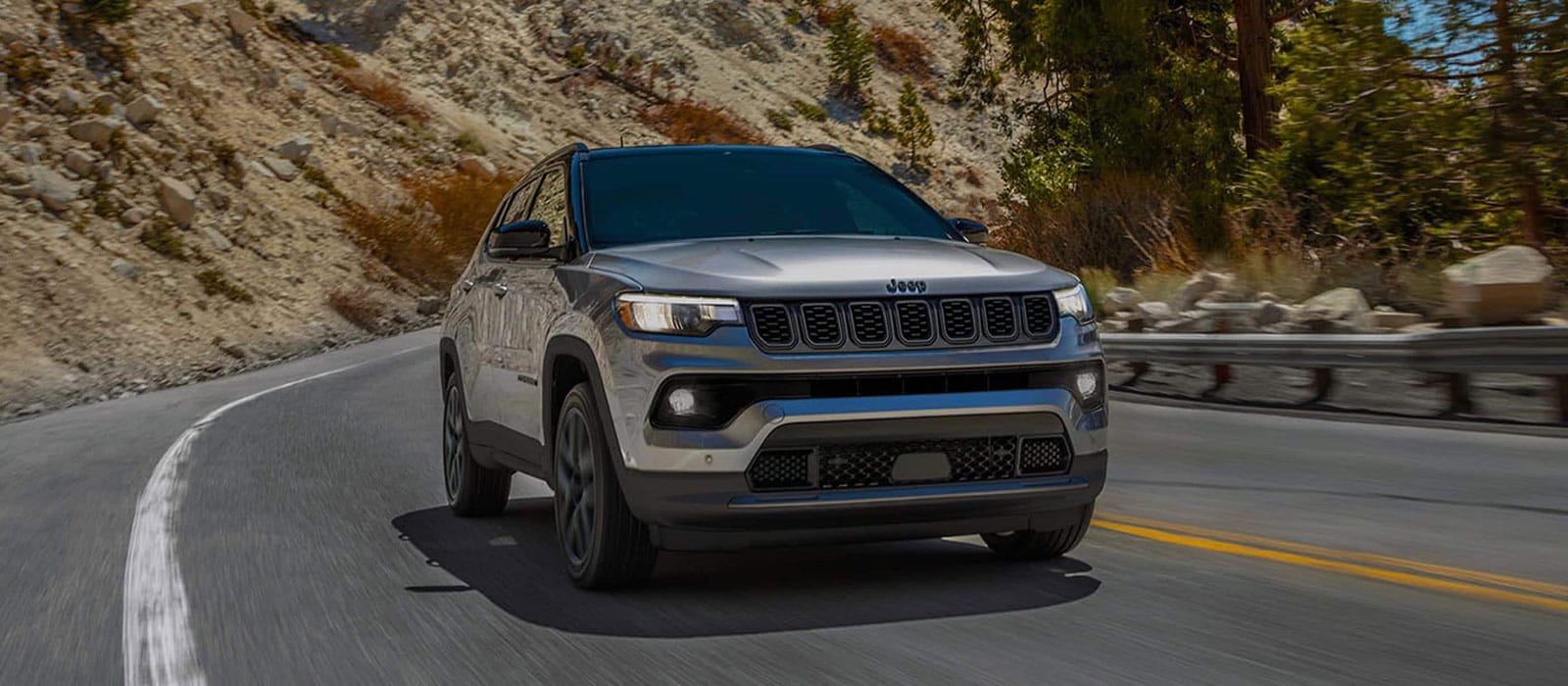 A silver Jeep Compass driving around a bend on the road.
