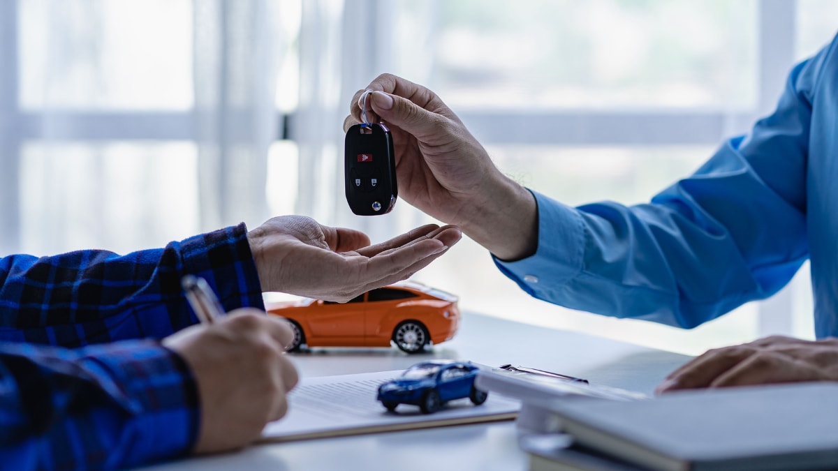Dealership salesman handing car keys to client as they sign a lease agreement