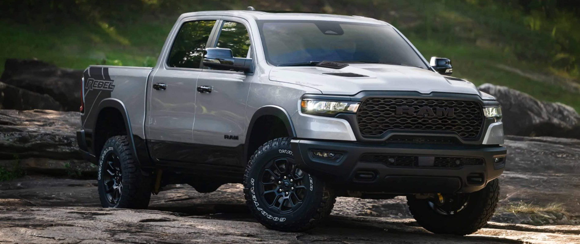 A silver RAM 1500 on a rocky area in a forest.