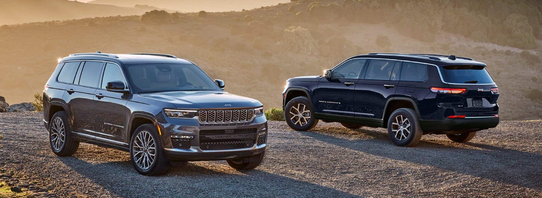 A pair of dark-colored Jeep Grand Cherokees parked on a dirt road over a cliff and facing opposite directions.